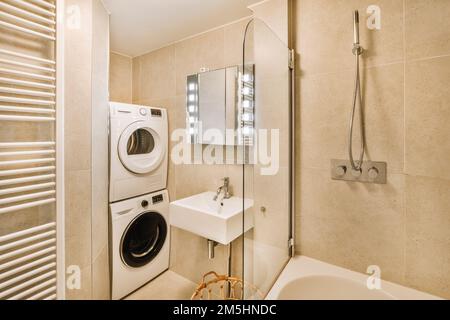 Ein Waschraum mit Waschmaschine und Badewanne in der Ecke, neben einer großen weißen Wanne Stockfoto