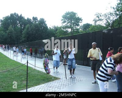 George Washington Memorial Parkway - Vietnam Veterans Memorial: Die Mauer. Die Menschen durchstöbern den Wandteil des Vietnam Veterans Memorial. Die Granitwände sind mit den Namen von mehr als 58.000 Männern und Frauen eingraviert, die ihr Leben in Vietnam gegeben haben oder die vermisst bleiben. The Mall, Washington, District of Columbia (38,891° N 77,048° W) Stockfoto