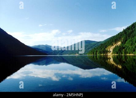 International Selkirk Loop - Reflexionen am Sullivan Lake. Berge und Himmel spiegeln sich im unberührten Wasser des Sullivan Lake wider. Östlich von MetaLine Falls, Washington, gelegen, bietet der See Angelmöglichkeiten, Bootstouren, Picknickplätze, Camping und Wanderwege mit Blick auf den See und die Selkirk Mountains. Sullivan Lake, Washington (48,808° N 117,292° W) Stockfoto