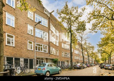 Eine Stadtstraße mit geparkten Autos und Fahrrädern auf dem Bürgersteig, vor einem Ziegelgebäude mit vielen Fenstern Stockfoto