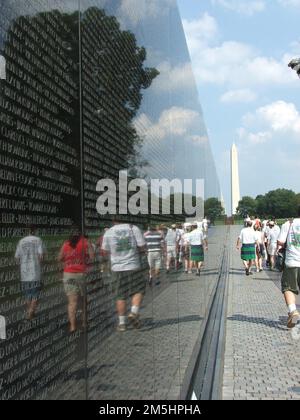 George Washington Memorial Parkway - Granitmauern des Vietnam Memorial. Eine Gruppe von Menschen geht am Vietnam Memorial vorbei. In der Ferne befindet sich das Washington Monument. Washington, District of Columbia (38,891° N 77,047° W) Stockfoto