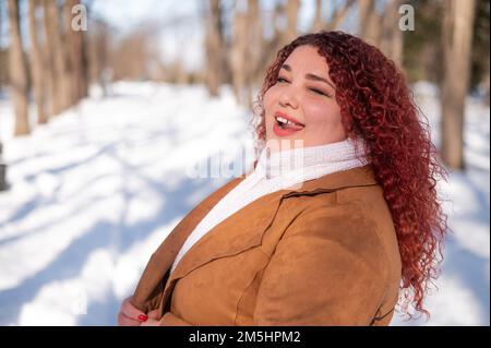 Eine fröhliche, fette Kaukasierin spaziert im Winter im Park. Stockfoto