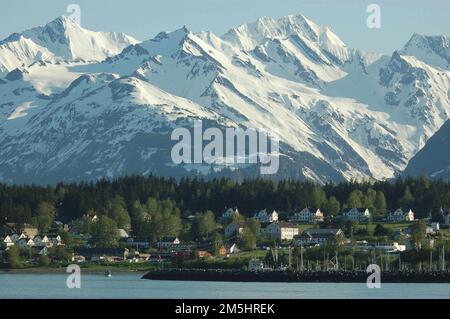 Haines Highway - Valley of the Eagles - Fort William H. Seward vom Picture Point. Die schneebedeckten Chilkat Mountains bilden die Kulisse für einen malerischen Blick auf die weißen Gebäude des historischen Fort William H. Seward auf der Fahrt vom Fährhafen in Richtung Innenstadt von Haines. Haines, Alaska Stockfoto