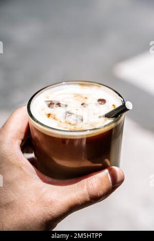 Eine Tasse Latte Cappuccino in der Hand auf der Straße der Stadt. Kaffeegetränk zum Mitnehmen. Hochwertiges Foto Stockfoto