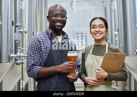 Porträt von zwei Brauern, die vor der Kamera lächeln, während sie gemeinsam Bier in der Brauerei verderben Stockfoto