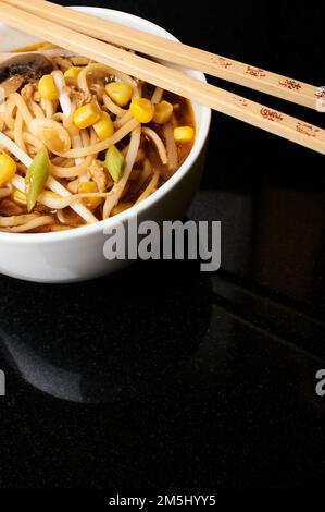 Eine Schüssel mit chinesischem Huhn und Zuckermaissuppe in einer weißen Schüssel mit Stäbchen auf schwarzem Hintergrund. Studioaufnahme. Stockfoto