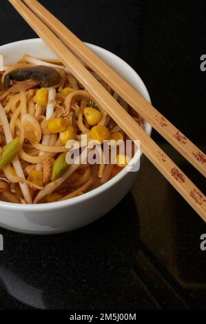 Eine Schüssel mit chinesischem Huhn und Zuckermaissuppe in einer weißen Schüssel mit Stäbchen auf schwarzem Hintergrund. Studioaufnahme. Stockfoto