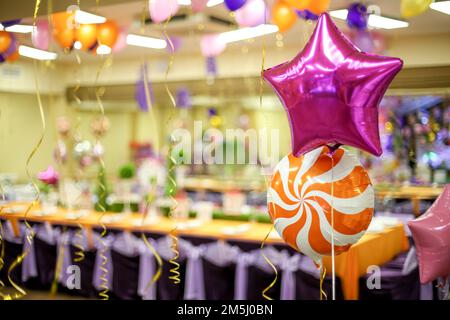 Zwei Ballons gefüllt mit Helium in Form eines Sterns und einem Lollipop vor dem Hintergrund einer dekorierten Festhalle Stockfoto