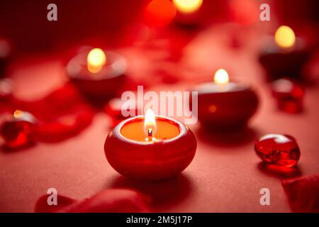 Romantische Dekoration für das Abendessen. Rote Kerzen, Blütenblätter, auf dem Tisch Stockfoto