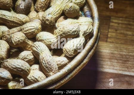 Erdnüsse in einer natürlichen Schüssel, die auf einem Holztisch ruht Stockfoto