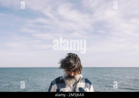 Das Gesicht des Mannes ist im Winter vor dem Hintergrund des Meeres mit Haaren bedeckt. Stockfoto