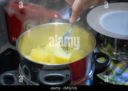 Kartoffeln in einem Dampfgarer, der gespalten wird, um zu sehen, ob sie gut gekocht sind. Stockfoto