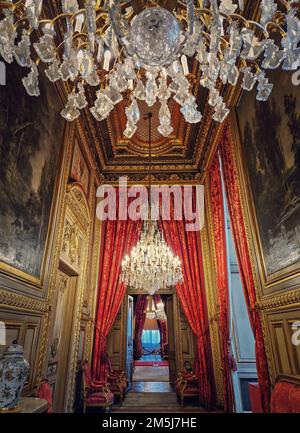 Wunderschön eingerichtete Napoleon Apartments im Louvre Palace. Königliche Familienzimmer mit kardinalroten Vorhängen, goldverzierten Wänden, Gemälden und Kristalltafel Stockfoto