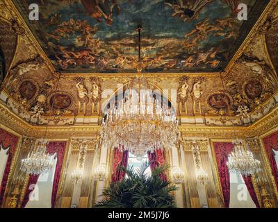 Wunderschön eingerichtete Napoleon Apartments im Louvre Palace. Königliche Familienzimmer mit kardinalroten Vorhängen, goldverzierten Wänden, Gemälden und Kristalltafel Stockfoto