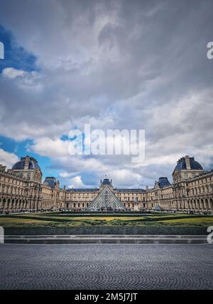 Blick auf den Louvre in Paris, Frankreich. Das historische Palastgebäude mit der modernen Glaspyramide in der Mitte, vertikaler Hintergrund Stockfoto