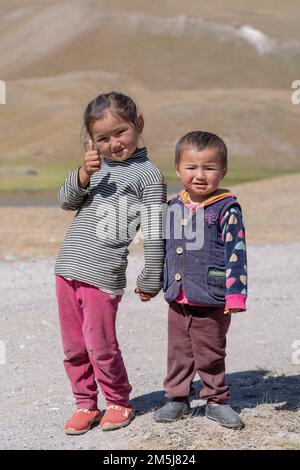 Achik Tash, Kirgisistan - 08 29 2019 : Kirgisische Bruder- und Schwesterkinder, die im Lenin Peak Basislager Händchen halten, lächeln und Daumen hoch halten Stockfoto