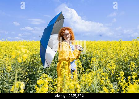 Junge Frau, die mit einem blauen Regenschirm posiert, an einem warmen Frühlingstag Stockfoto