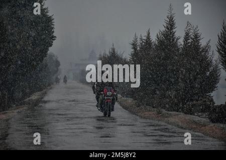 Ein Motorradfahrer fährt während des ersten Schneefalls der Saison in Srinagar entlang der Straße. Stockfoto