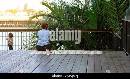 BANGKOK, THAILAND-FEBRUAR 23,2020:Unidentifizierte Großmutter kümmert sich um die Fütterung ihres Enkels Essen und Wasser, während faulenzen auf der Terrasse am Fluss in Hi Stockfoto