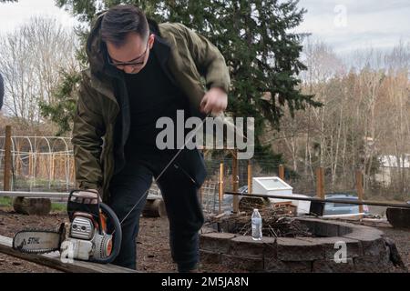 KITSAP COUNTY, Washington (18. März 2022) – USA Navy Yeoman Seaman Daniel Kendall aus Salt Lake City, dem Flugzeugträger der Nimitz-Klasse USS Theodore Roosevelt (CVN 71) zugeteilt, startet eine Kettensäge während einer gemeinnützigen Veranstaltung am 18. März 2022. Theodore Roosevelt unterzieht sich einer geplanten zusätzlichen Anlegephase an der Puget Sound Naval Shipyard und der Intermediate Maintenance Facility, wo das Schiff planmäßig gewartet und modernisiert wird. Stockfoto