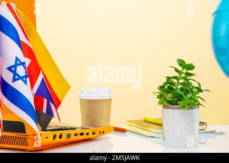 Internationale Online-Bildung. Laptop, Notebooks, eine Kugel, eine Tasse Kaffee und Flaggen aus verschiedenen Ländern auf beigefarbenem Hintergrund mit Kopierbereich. Konz Stockfoto