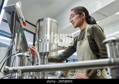 Arbeiterin, die den Arbeitsablauf von Geräten während ihrer Arbeit in der Brauerei steuert Stockfoto