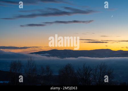 Winteruntergang im mährisch-schlesischen Beskiden in der Tschechischen Republik in der Nähe der polnischen Grenze, des farbenfrohen Himmels und der Berggipfel über dem nebligen Tal Stockfoto