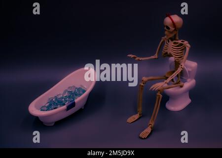 Ein Skelett mit rotem Stirnband und Schleife sitzt auf einer Toilette und macht sich bereit, ein Bad zu nehmen. Stockfoto