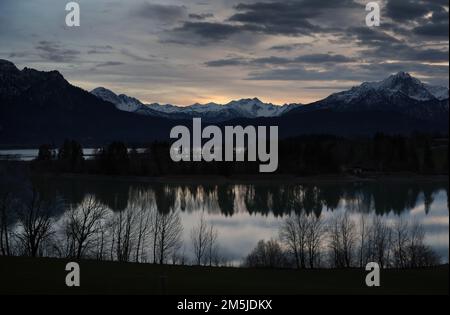 29. Dezember 2022, Bayern, Roßhaupten: Im Sonnenuntergang spiegeln sich Bäume im Forggensee am Alpenrand wider. Foto: Karl-Josef Hildenbrand/dpa Stockfoto