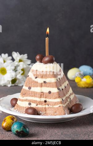 Traditionelles Oster-Hüttenkäse-Dessert mit Schokolade sowie farbenfrohe Eier auf grauem Hintergrund, vertikales Bild Stockfoto