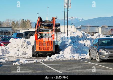 Baggerlader beim Schneeräumen auf einem Parkplatz im Einkaufszentrum. Pitt Meadows, B.C., Kanada. Stockfoto