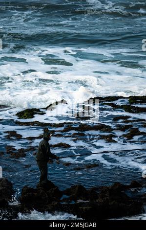 Silhouette eines Mannes, der bei Flut im Atlantischen Ozean fischen will. Fischfang bei außergewöhnlichen Wetterbedingungen. Stockfoto