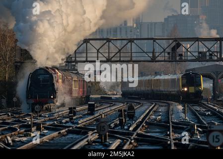 Alt und neu, eine elektrische Lokomotive, neben der Dampfeisenbahn 46233, die sich an einem kalten Dezembermorgen der Clapham Junction nähert, die Londoner Skyline im Hintergrund Stockfoto