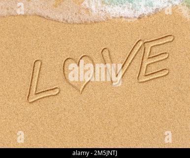 Worte in Strandsand geschrieben. Das Wort LIEBE im Sand am Strand mit dem Ozean als Hintergrund geschrieben. Liebe ist alles, was du brauchst. Jeder liebt das Stockfoto