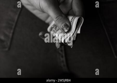 Frau Hand Geld nimmt, aus Jeans Gesäßtasche. Frau Geld versteckt hinter ihrem Rücken. Dollar Banknoten Nahaufnahme Stockfoto