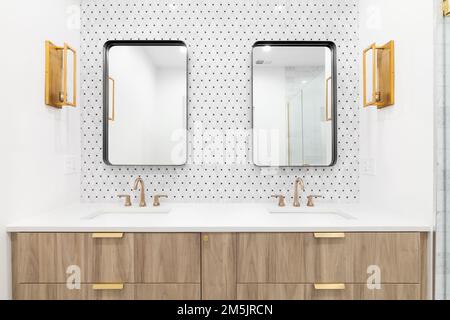 Ein wunderschönes Badezimmer mit einem schwimmenden Schrank aus Holz, goldenem Wasserhahn und Lampen, Mosaikfliesen an der Wand und rechteckigen Spiegeln. Stockfoto