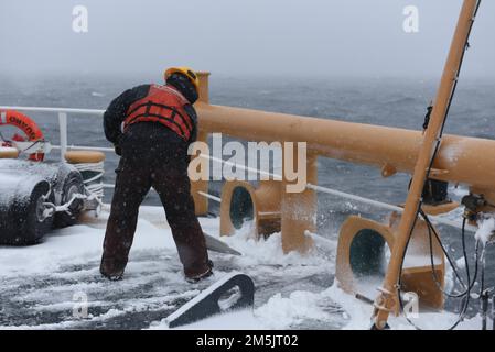 USA Küstenwache Petty Officer 1. Klasse Timothy Koscielny, ein Bootsmann an Bord der Küstenwache Cutter Spar, räumt die Wetterdecks vom Schnee, während sie im Golf von Sankt-Lorenz unterwegs ist, 20. März 2022. Spar und ihre Crew reisen nach Duluth, Minn. nach einer einjährigen Wartungszeit in Baltimore. Stockfoto