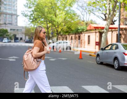 Eine schöne Aufnahme einer lächelnden jungen Frau mit einem Rucksack, die die Straße überquert Stockfoto