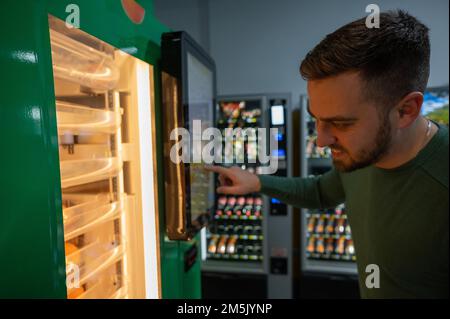 Ein weißer Mann kauft frisch gepressten Orangensaft aus dem Automaten. Stockfoto