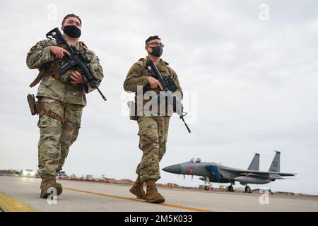 Zwei Verteidiger, die der Patrouille der 18. Sicherheitseinheit zugeteilt sind, umzingeln die 44. Fighter Squadron F-15C Eagles, die auf der Fluglinie der Japan Air Self-Defense Force Tsuiki Air Base am 21. März 2022 geparkt sind. Das Flugzeug kam in Fukuoka für das Umsiedlungsprogramm für Flugschulungen an, das die Betriebsbereitschaft erhöht und die Interoperabilität mit unseren japanischen Verbündeten verbessert. Stockfoto