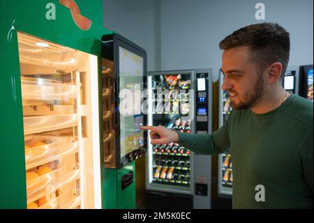 Ein weißer Mann kauft frisch gepressten Orangensaft aus dem Automaten. Stockfoto