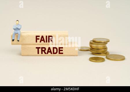 Geschäftskonzept. Auf dem Tisch liegen Münzen, Holzteller mit der Inschrift "FAIR TRADE". Eine Figur eines Geschäftsmannes sitzt auf den Würfeln. Stockfoto