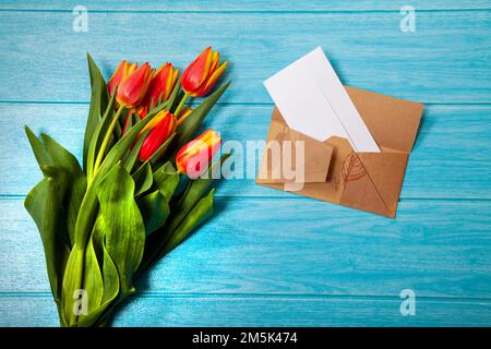 Eine Draufsicht der Tulpenblüten mit einem Umschlag auf weißem Holzhintergrund Stockfoto