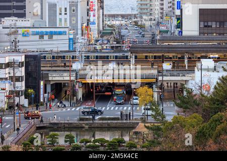 Akashi, Japan - 29. Dezember 2022: Leichter Verkehr durchquert die Kreuzung in der Innenstadt, während die Züge über dem Bahnhof abfahren Stockfoto