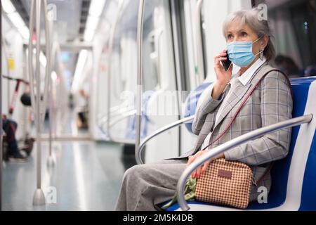 Ältere Frau in Maske, die im U-Bahn-Zug telefoniert Stockfoto