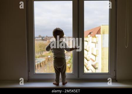 Einsames Kind, das auf dem Fensterbrett steht. Gefahrensituation, Sturzgefahr. Stockfoto