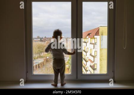 Einsames Kind, das auf dem Fensterbrett steht. Gefahrensituation, Sturzgefahr. Stockfoto