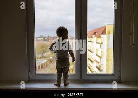 Einsames Kind, das auf dem Fensterbrett steht. Gefahrensituation, Sturzgefahr. Stockfoto