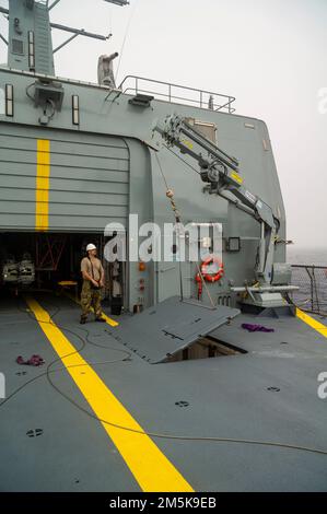 Matrosen an Bord des Patrouillenschiffs HDMS Triton der Königlichen Dänischen Marine heben mit einem Hydraulikkran einen Außenbordmotor aus einem Lagerfach. Stockfoto