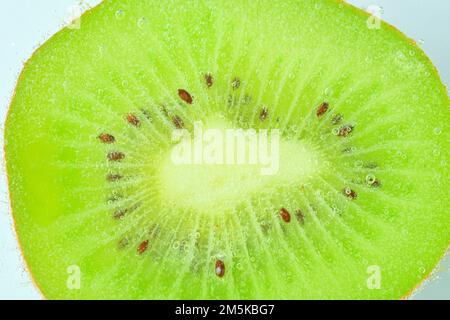 Nahaufnahme von Kiwifrüchten in flüssiger Flüssigkeit mit Blasen. Eine Scheibe grüne, reife Kiwis in Mineralwasser. Saftige Kiwis in kohlensäurehaltigem Wasser. Makrobild. Stockfoto